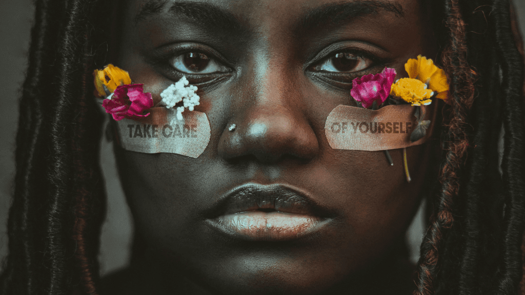 Close up of a young woman with a bandaid on each cheek with flowers tucked into the bandaids.