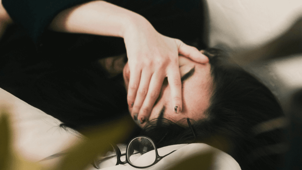 A woman laying down covering her face with her hand to cry.