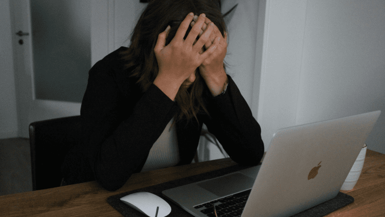 A woman sitting at a desk with her head in her hands.