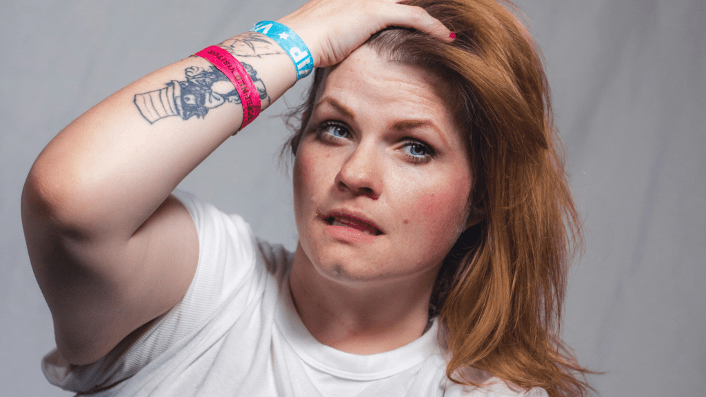A young woman running her hand through her hair, looking confusedly into the camera.