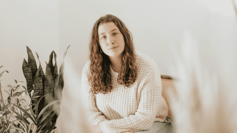 Young brunette sitting in a white sweater looking calmly at the camera waiting for her trauma informed care.