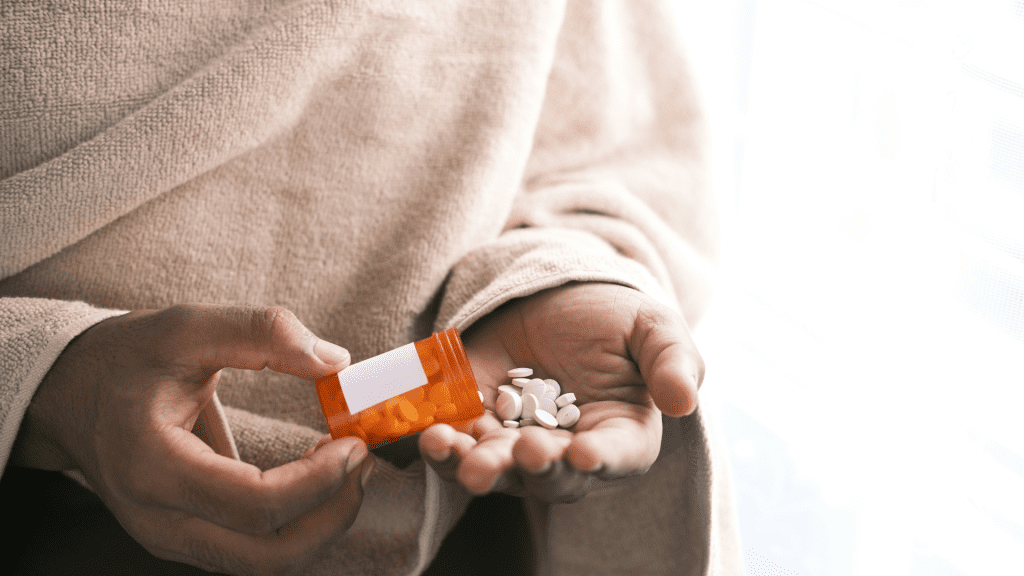 Close up image of a woman pouring pills out of an orange presciption bottle into her hand.