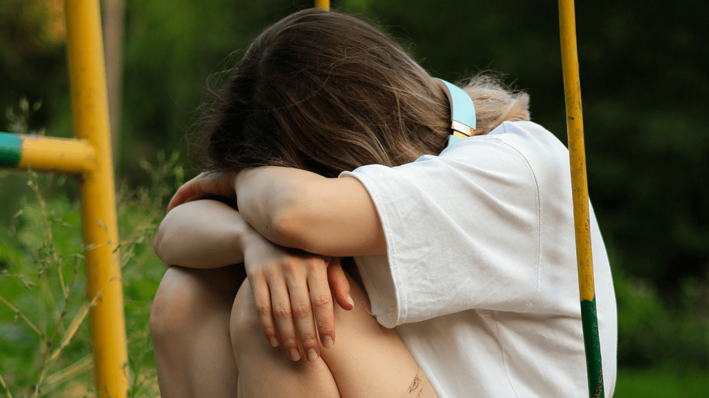 A young woman sitting head-down on a swing.